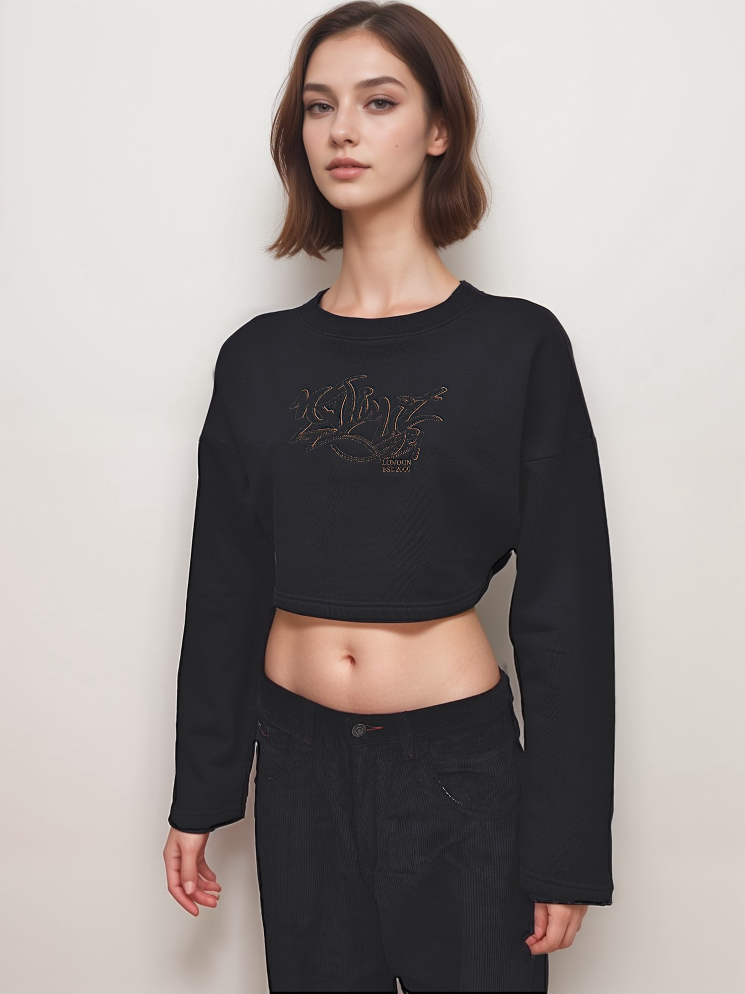 A woman wearing a black cropped pullover sweatshirt with gold embroidery, paired with black shorts.